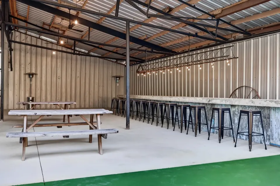 The covered pavilion with picnic tables and a long outdoor bar lined with black metal stools